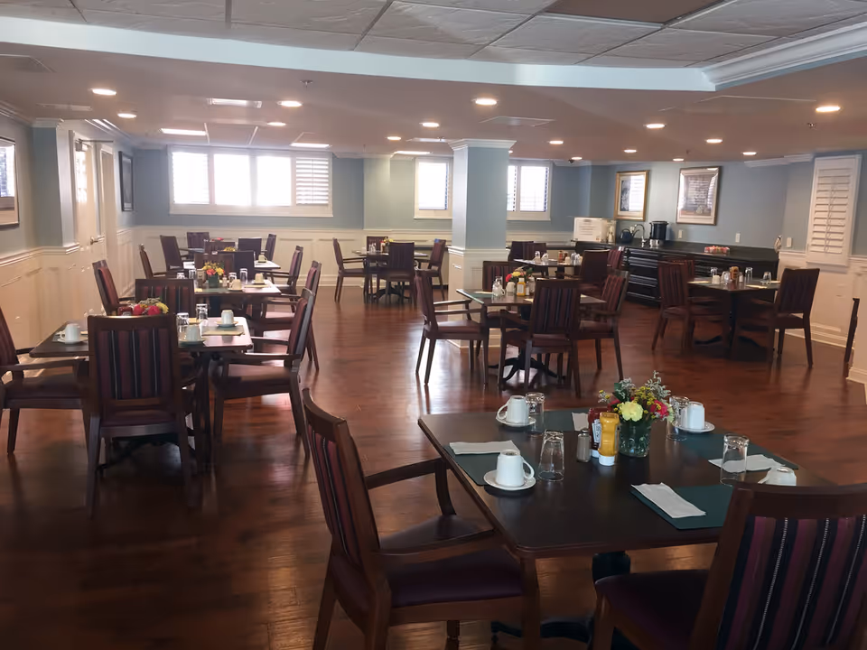 Spacious dining room with multiple set tables and chairs, place settings, and floral centerpieces.