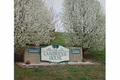A large stone sign for Cambridge House with two smaller signs on either side reading 'Delaware' and 'Virginia', surrounded by grass and blooming trees in the background.