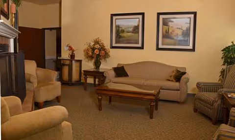 Cozy lounge area with beige sofa, armchairs, coffee table, and framed paintings.
