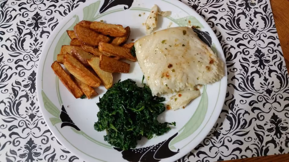 Plate with fish, roasted potatoes, and greens on a patterned tablecloth