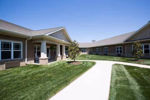 Exterior view of a single-story senior living facility with curved walkway and green lawn.