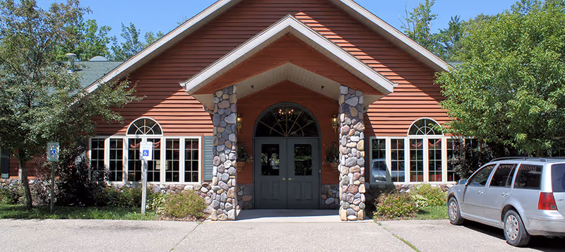 Front exterior view of North Haven Assisted Living facility with a peaked roof, stone pillars, large windows, and a parked silver car on the right side.