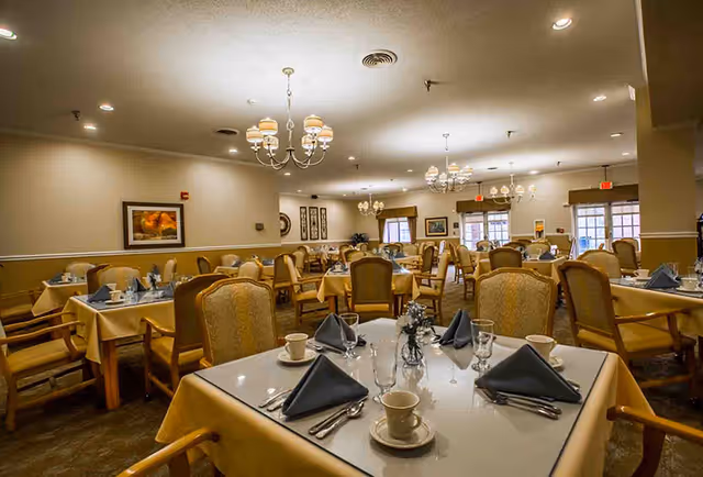 Spacious dining room with multiple tables set with napkins, cups, and silverware under chandeliers.