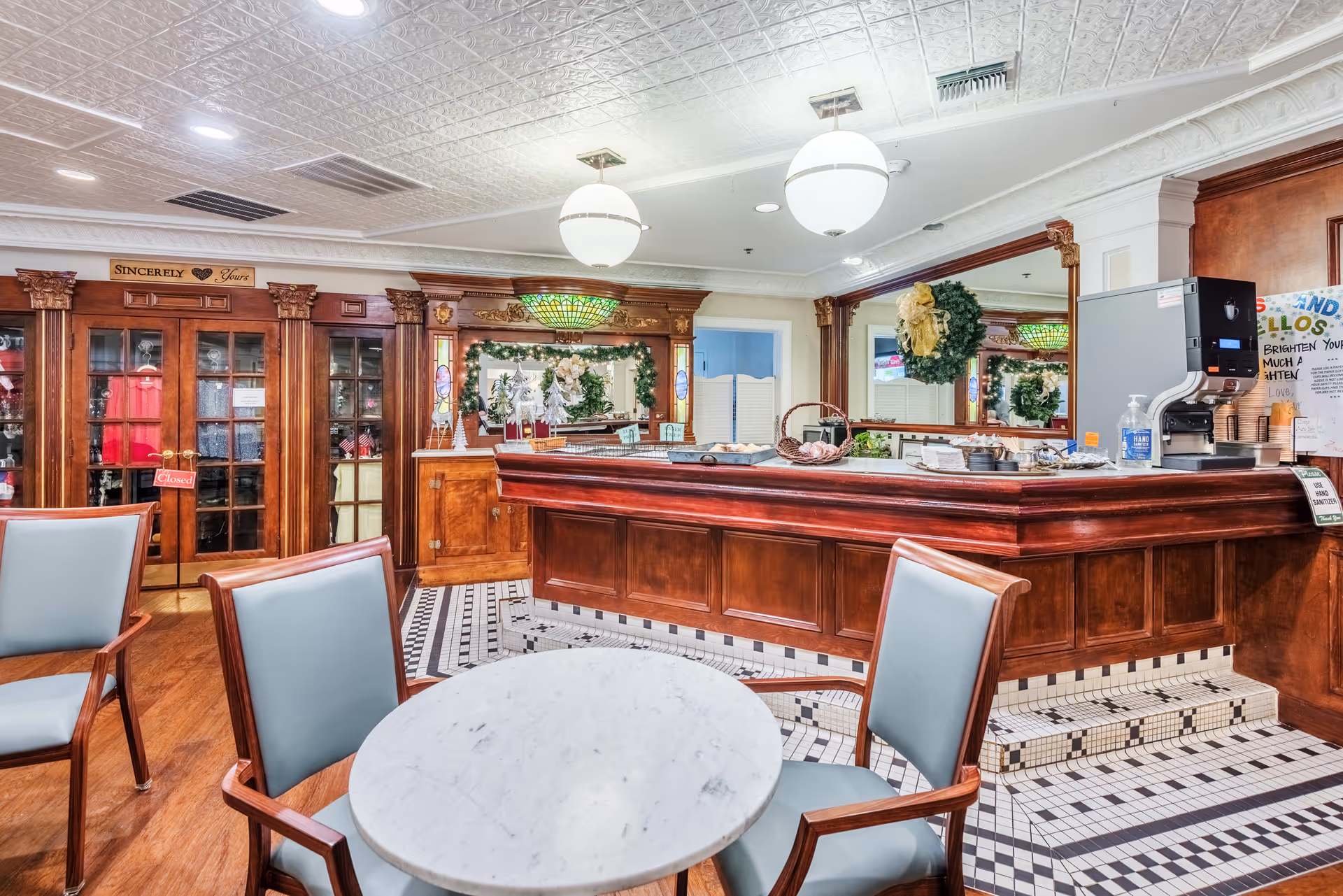 Reception area with a wooden front desk, round marble table with chairs, stained-glass accents and holiday wreath decorations.
