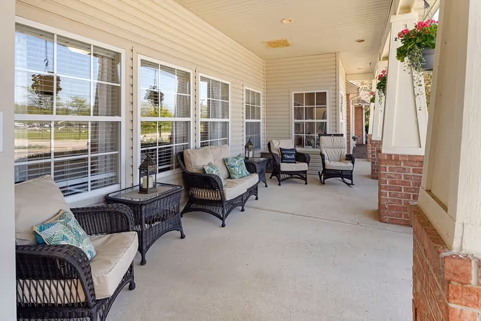 Covered front porch with wicker seating, side tables, and hanging flower baskets along windows.