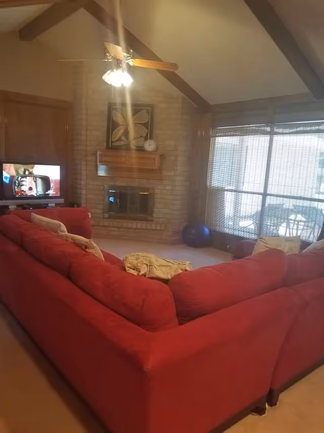 Red sectional sofa dominates a cozy living room with brick fireplace and large windows.