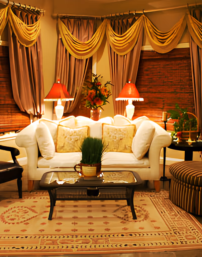 Decoratively furnished living room with a white sofa, coffee table, table lamps, draped curtains and area rug.