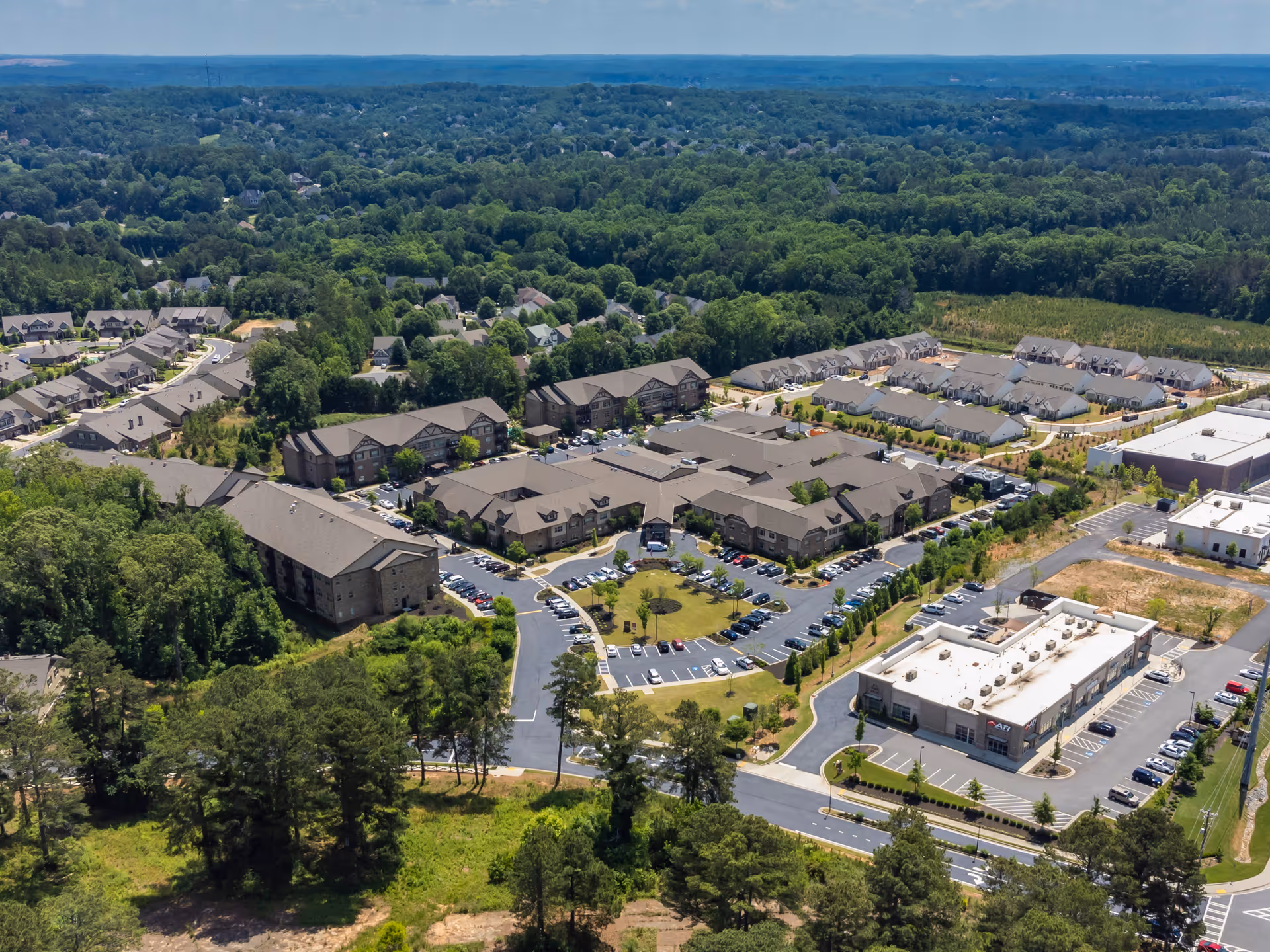 Aerial view of Celebration Village Forsyth senior living facility surrounded by trees and greenery, showing multiple buildings, parking lots, and roads within the complex.