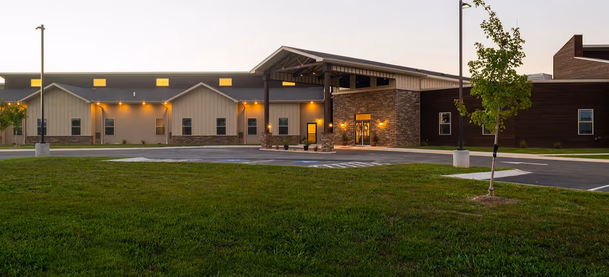 Exterior view of a senior living facility with an illuminated entrance and green lawn.