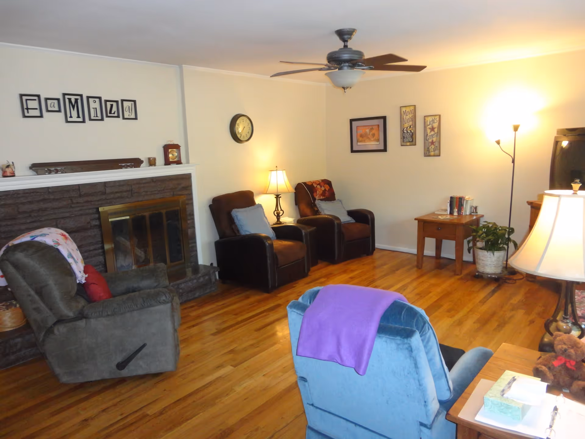 Cozy living room with several recliner chairs, a fireplace, hardwood floors, and lamps.