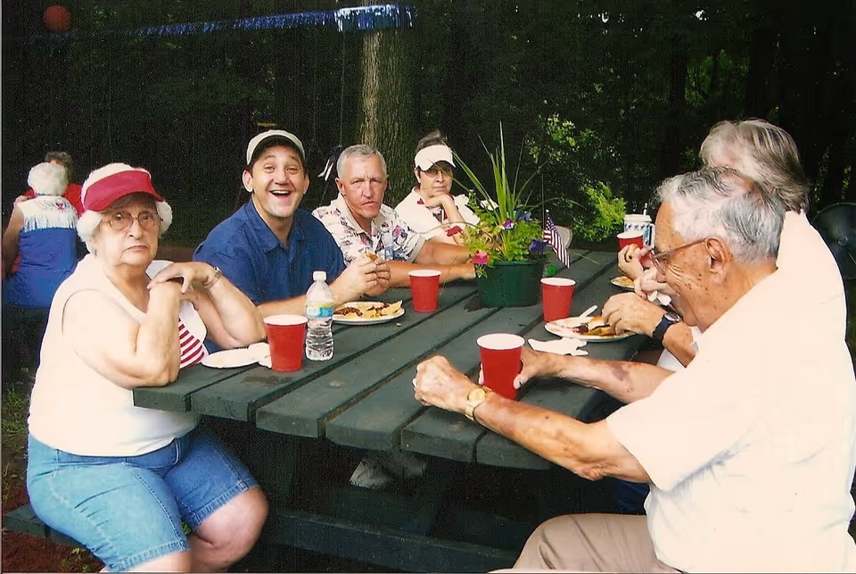A group of older adults sitting around a green outdoor picnic table eating and drinking.