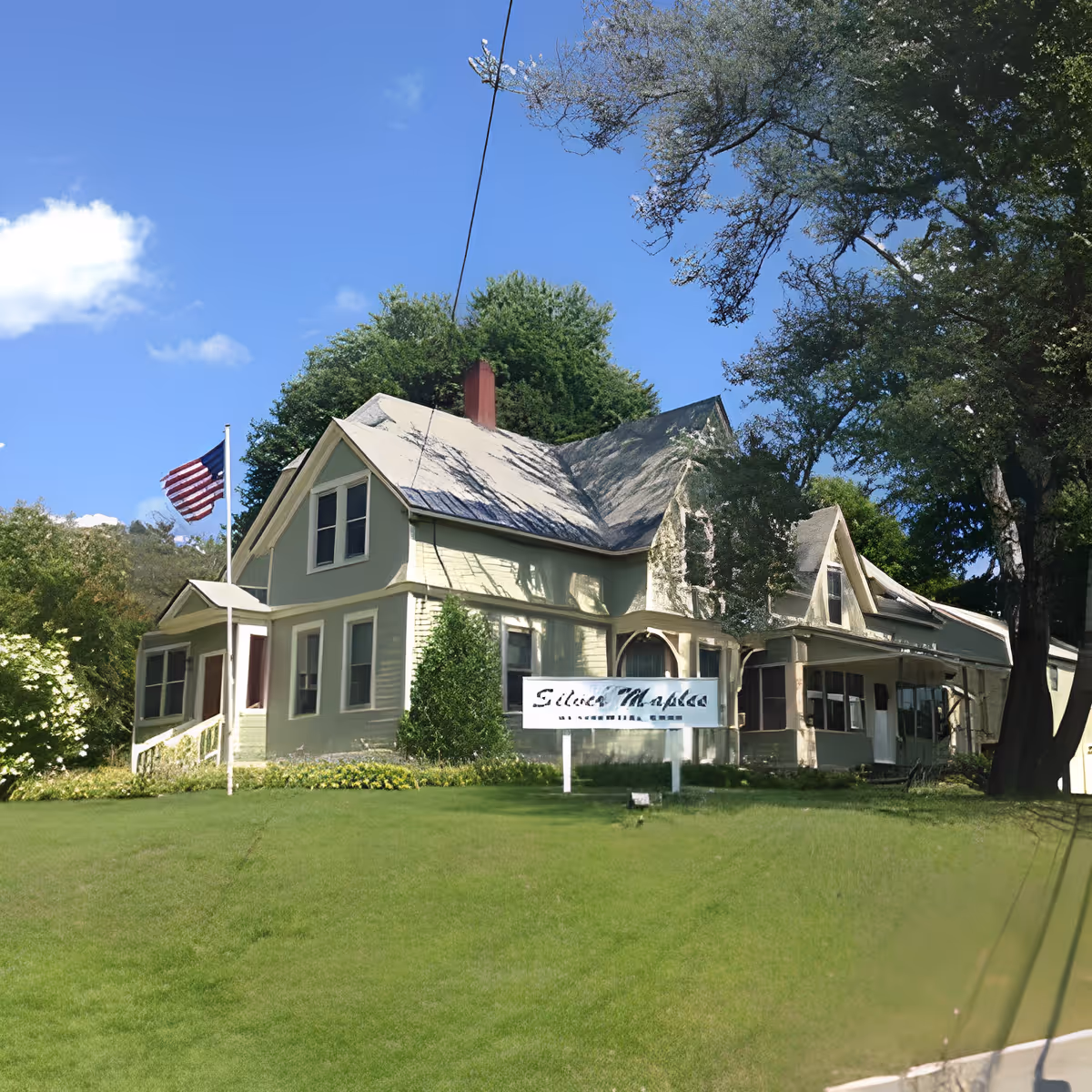 Light-green Victorian-style building with a lawn, American flag, and a 'Silver Maples' sign in front.