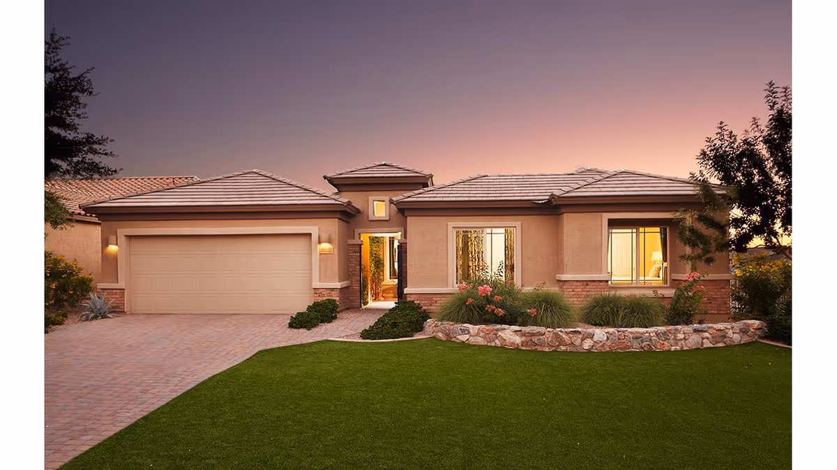 Front exterior view of a single-story house at sunset with a well-maintained lawn, stone-bordered flower beds, and a two-car garage.