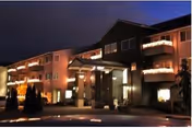 Exterior view of Canterbury Manor at night, showing a multi-story building with balconies and warm lighting illuminating the entrance and facade.
