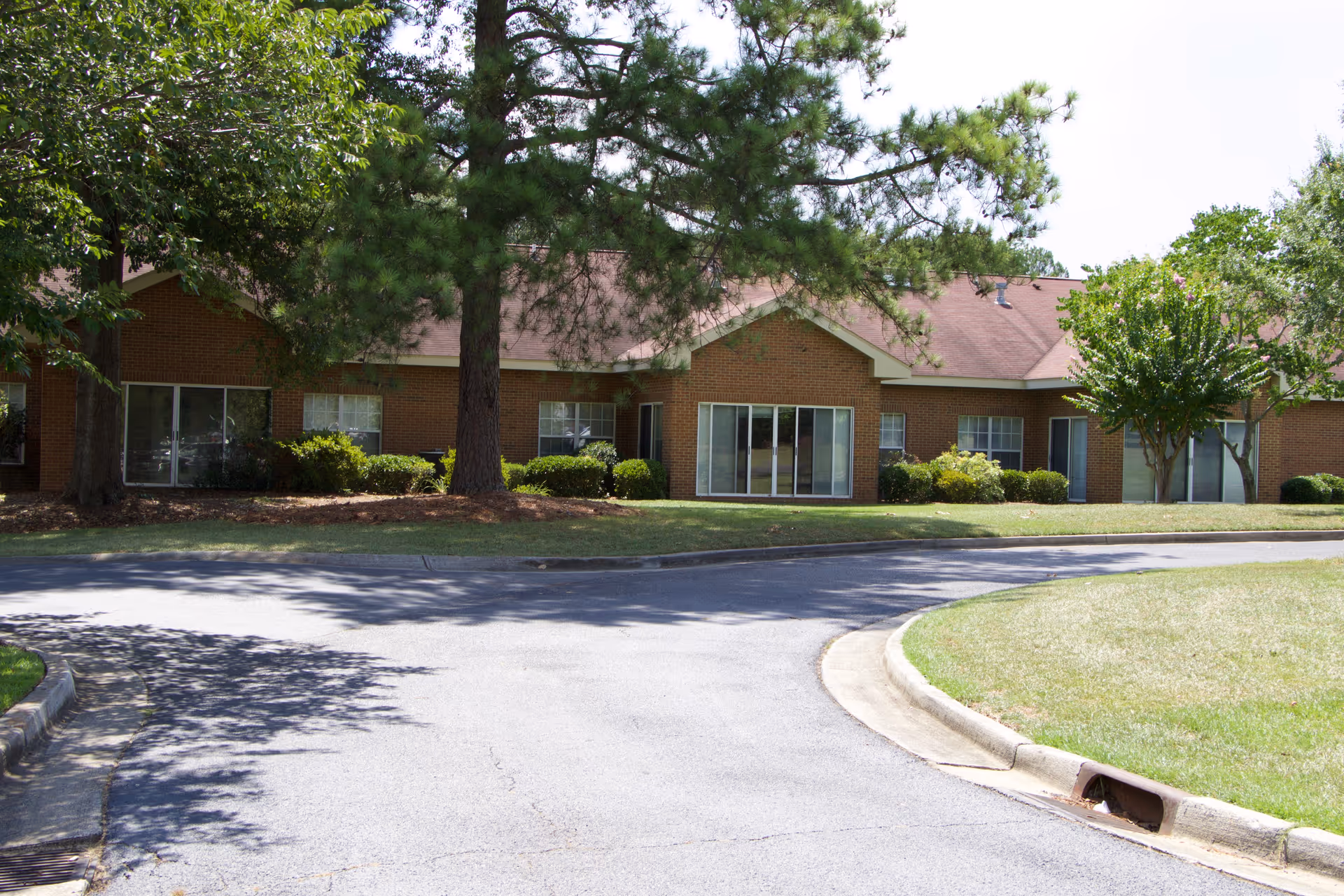 Front view of a single-story brick building with large windows, trees, lawn and a curved driveway.