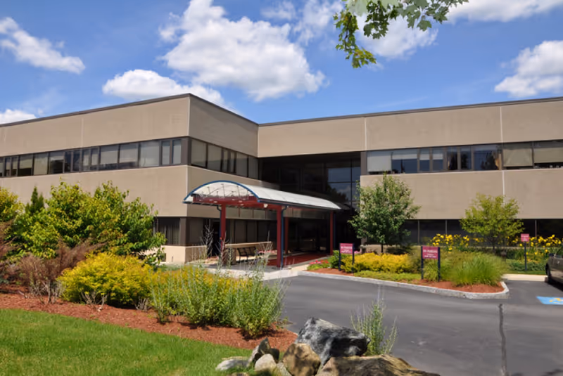 Front exterior of a two-story assisted living building with a covered entrance, landscaped beds, and a driveway.