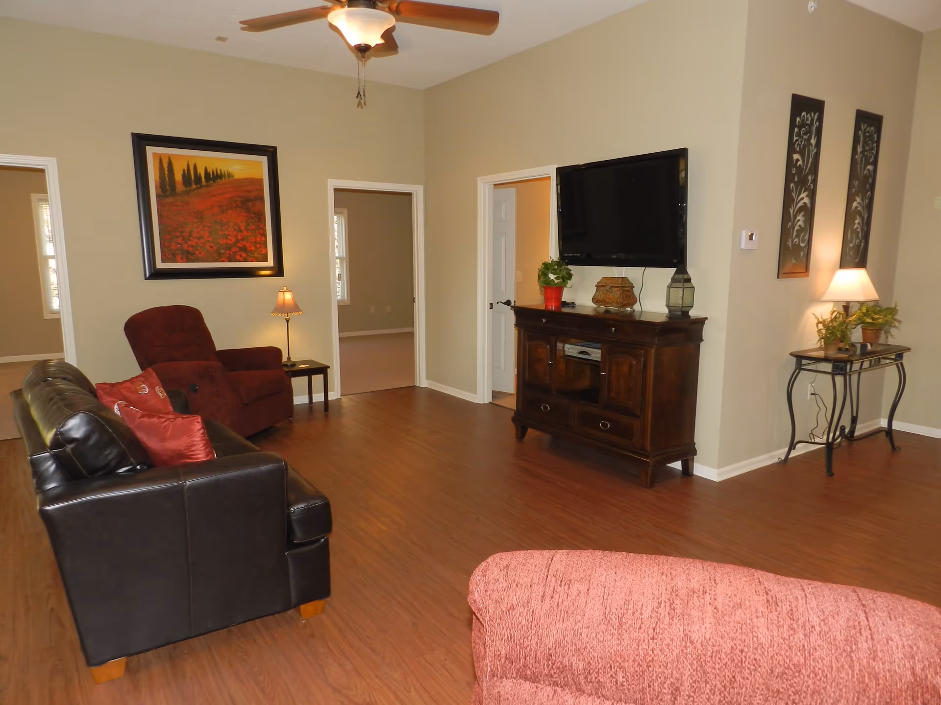 Spacious living room with a leather sofa, recliner, wall-mounted TV on a wooden cabinet, and hardwood floors.
