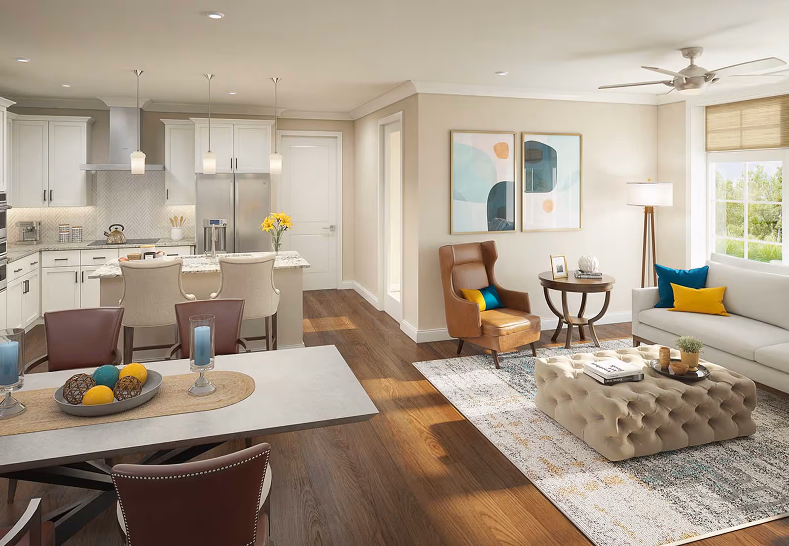 A bright and modern open-concept living space featuring a kitchen with white cabinetry, stainless steel appliances, and a granite island with three beige bar stools. Adjacent to the kitchen is a dining area with a table set with decorative items and four brown chairs. The living room area includes a white sofa with colorful pillows, a tufted ottoman coffee table, a brown leather armchair, a round side table with a lamp, and two abstract art pieces on the wall. Large windows allow natural light to fill the room, highlighting the wood flooring and neutral wall colors.
