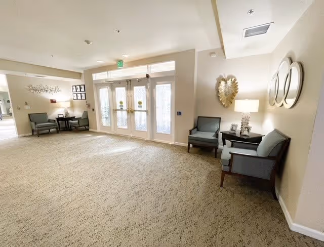 Bright carpeted lobby with double glass entry doors, upholstered chairs, side tables and wall decorations.