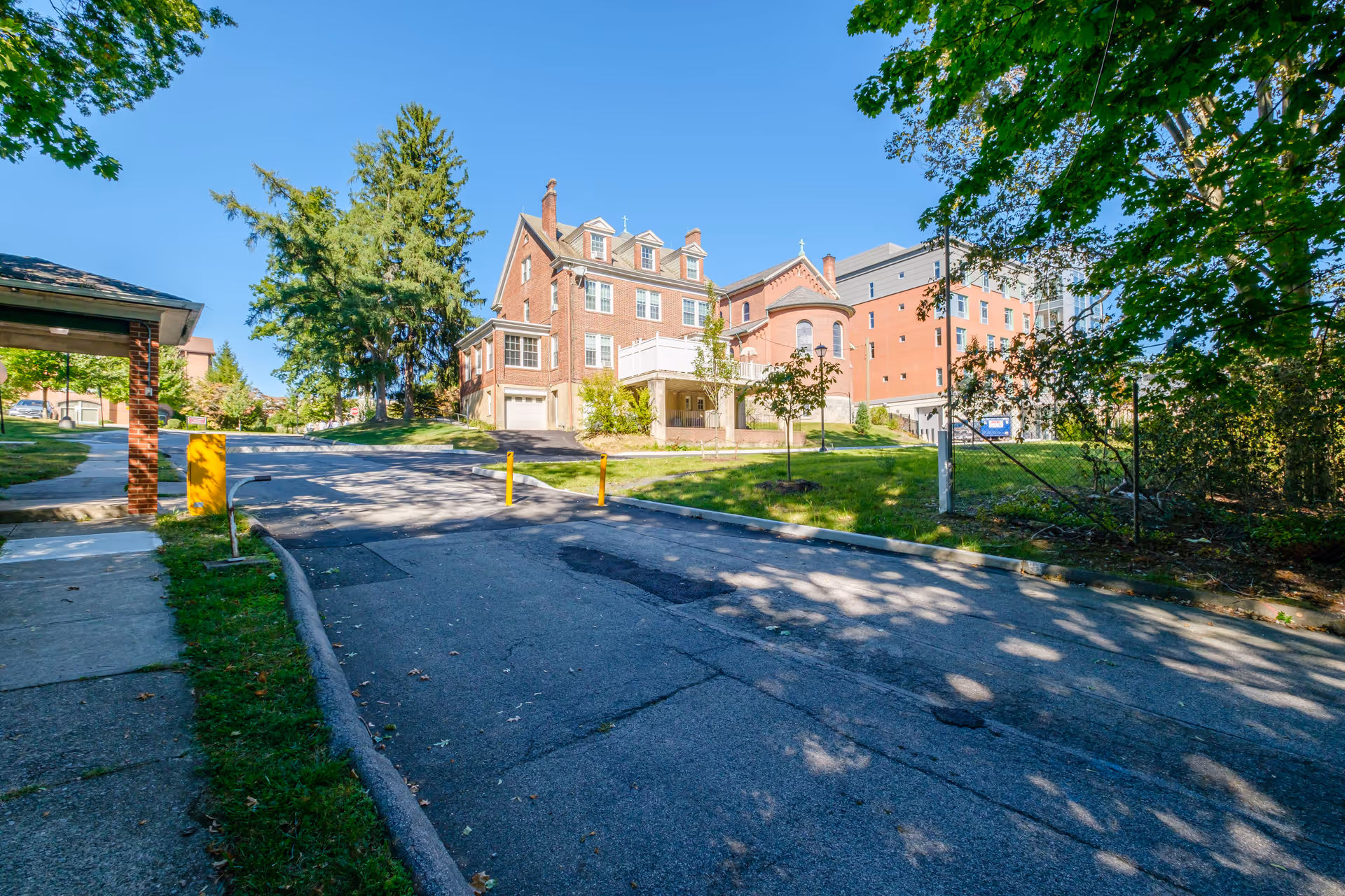 Exterior view of Meadowview Assisted Living Facility showing a large brick building with multiple windows and a sloped roof under a clear blue sky. The building is surrounded by green trees and grass, with a paved driveway and sidewalk in the foreground.