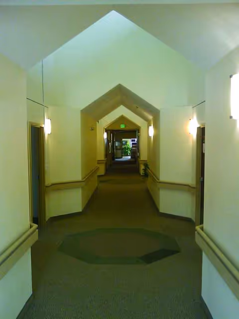 Long interior hallway with arched ceilings and wall lamps in a senior living facility.