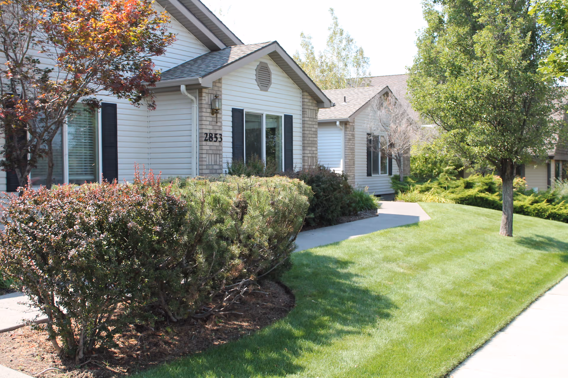 Front exterior of a single-story residential unit (address 2853) with siding, shrubs, a green lawn, and a sidewalk.