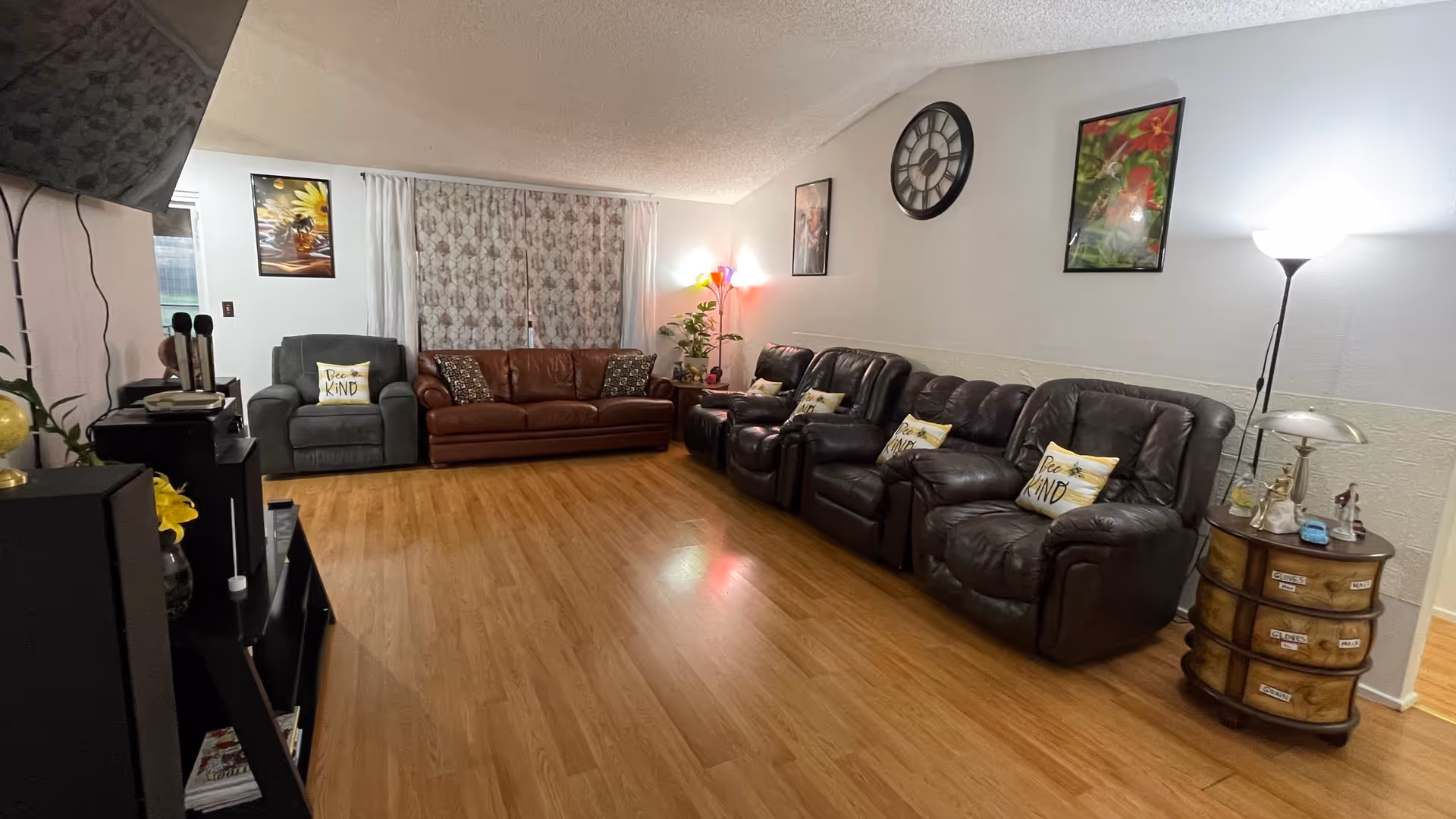 Spacious living room with several leather recliner chairs and sofas arranged along the walls, hardwood floor, side tables, lamps, and wall art.
