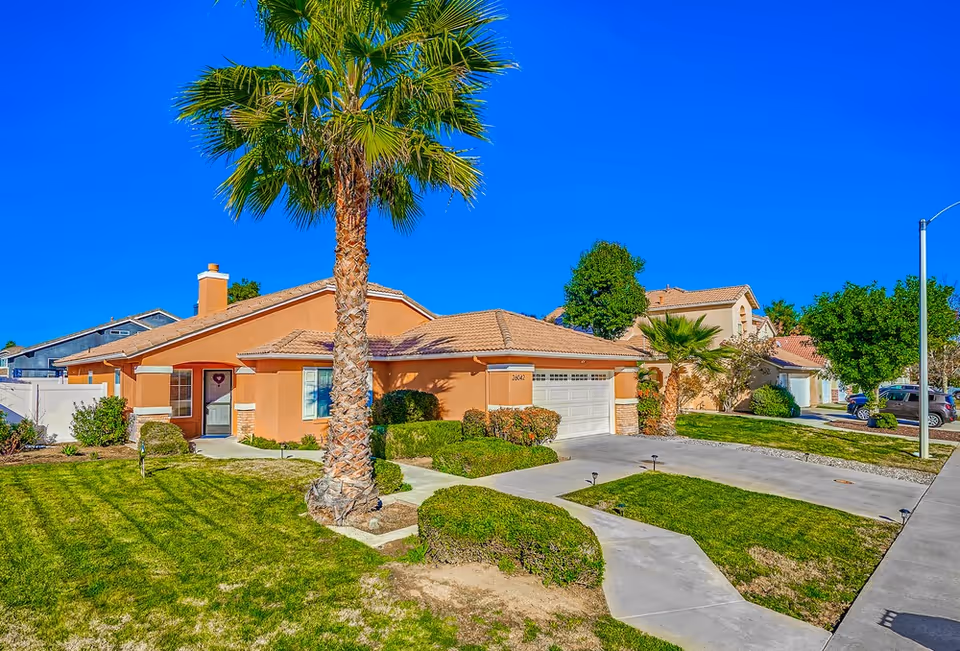 Orange single-story assisted living home with palm tree, driveway, and manicured lawn.