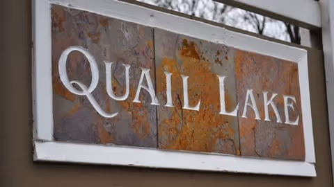 Rusty slate sign reads QUAIL LAKE mounted on a white frame.