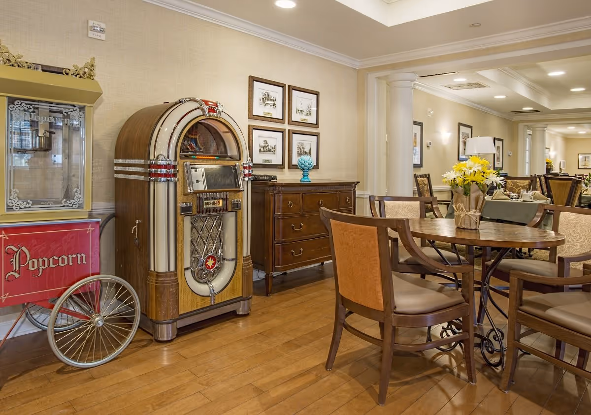 Round wooden dining table and chairs in a communal dining room with a vintage jukebox and popcorn cart against the wall.