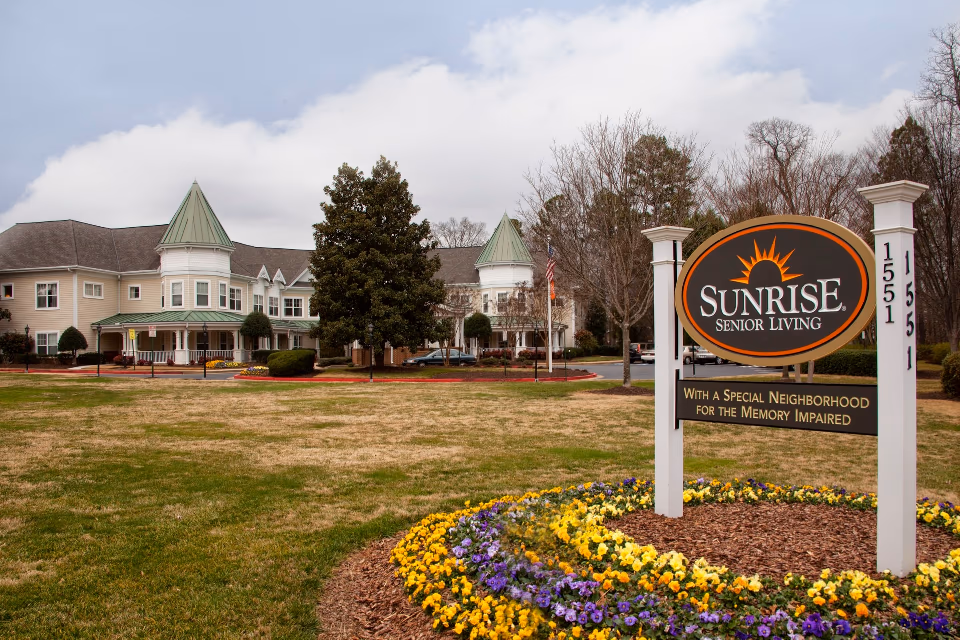 Exterior view of the Sunrise Senior Living building and entrance sign with a landscaped flower bed in front.