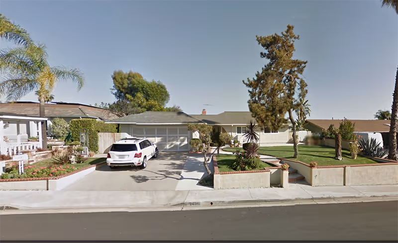 Single-story care facility exterior with driveway, car, and landscaped front yard.
