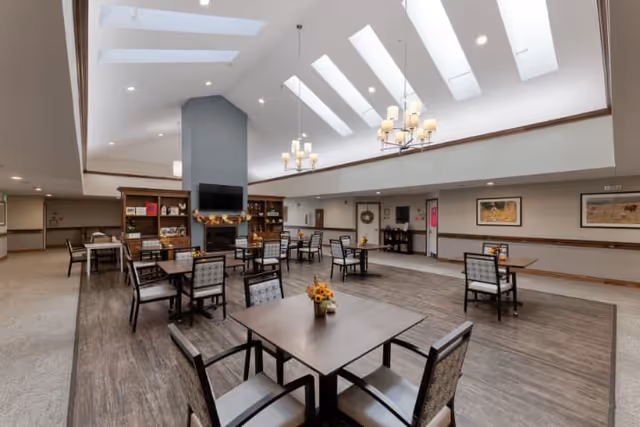 Spacious dining room with multiple tables and chairs, skylights, chandeliers, and a fireplace with shelving.