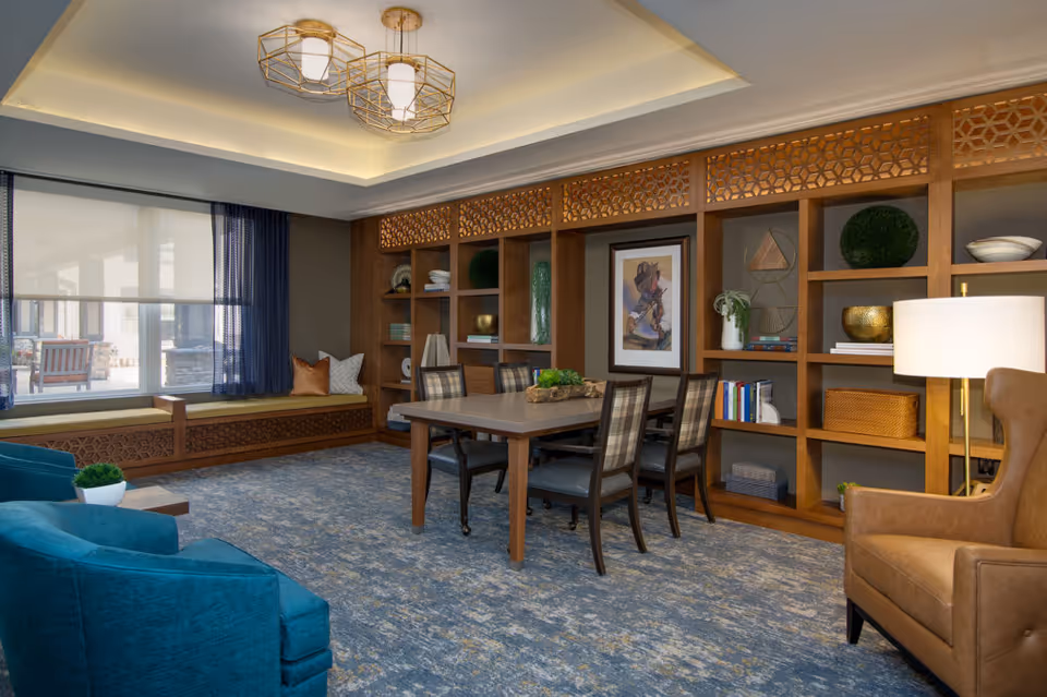 Well-appointed communal living room with built-in shelving, a central table and chairs, and comfortable seating under decorative lighting.