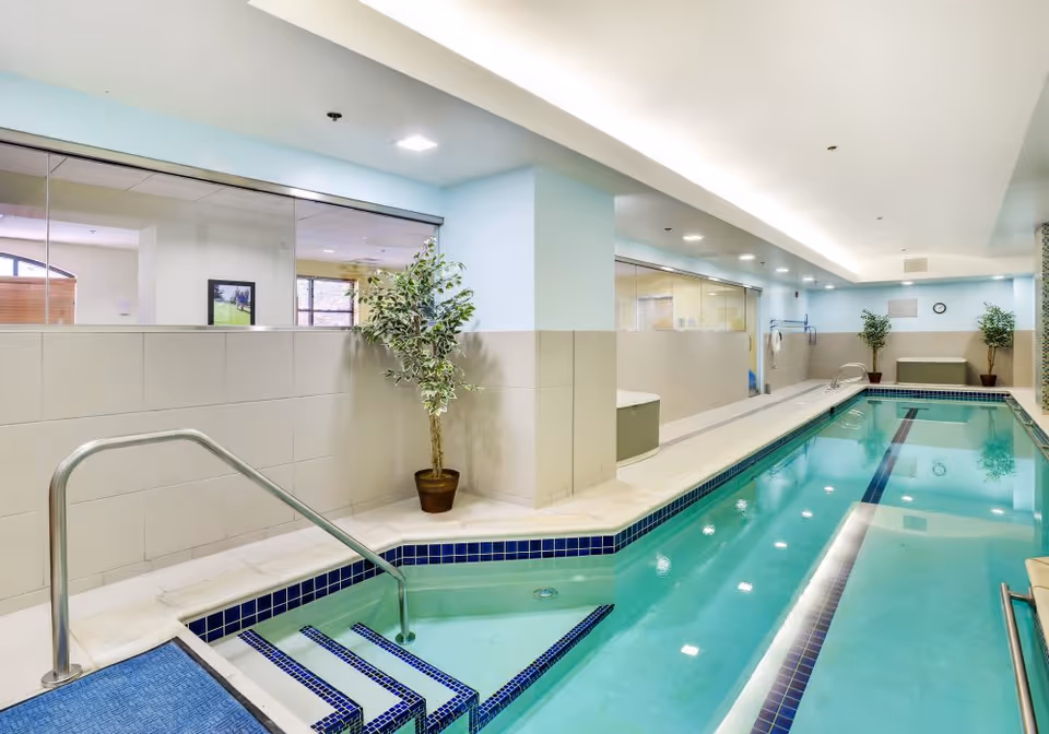 Bright indoor lap pool with tiled steps, stainless handrails, potted plants and glass partition walls.