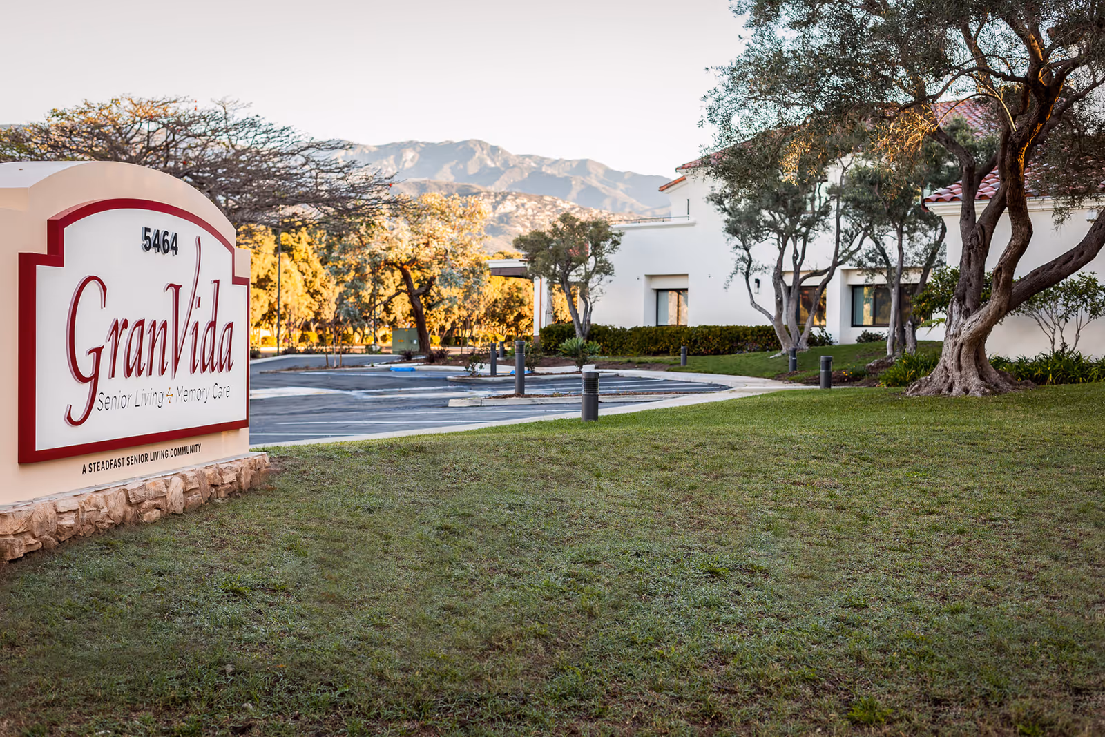 Entrance sign reading 'GranVida Senior Living & Memory Care' on a lawn with the facility building, trees, and mountains in the background.