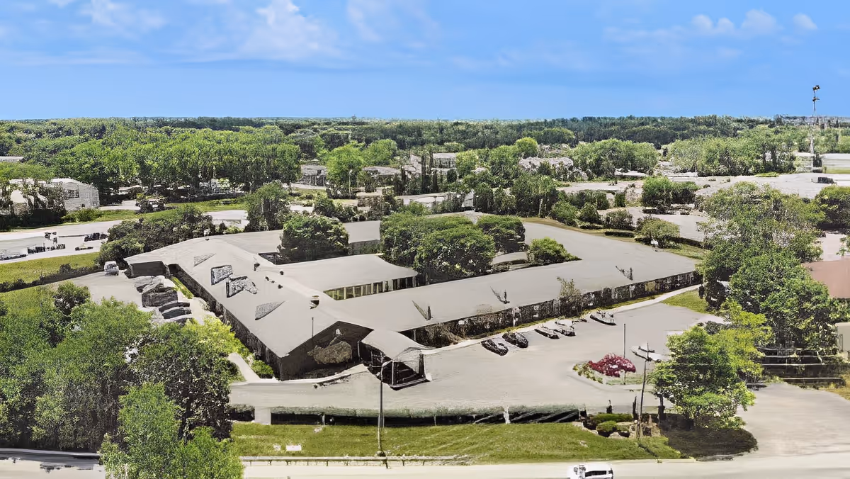 Aerial view of a single-story senior living complex with a parking lot, landscaped grounds, and surrounding trees.
