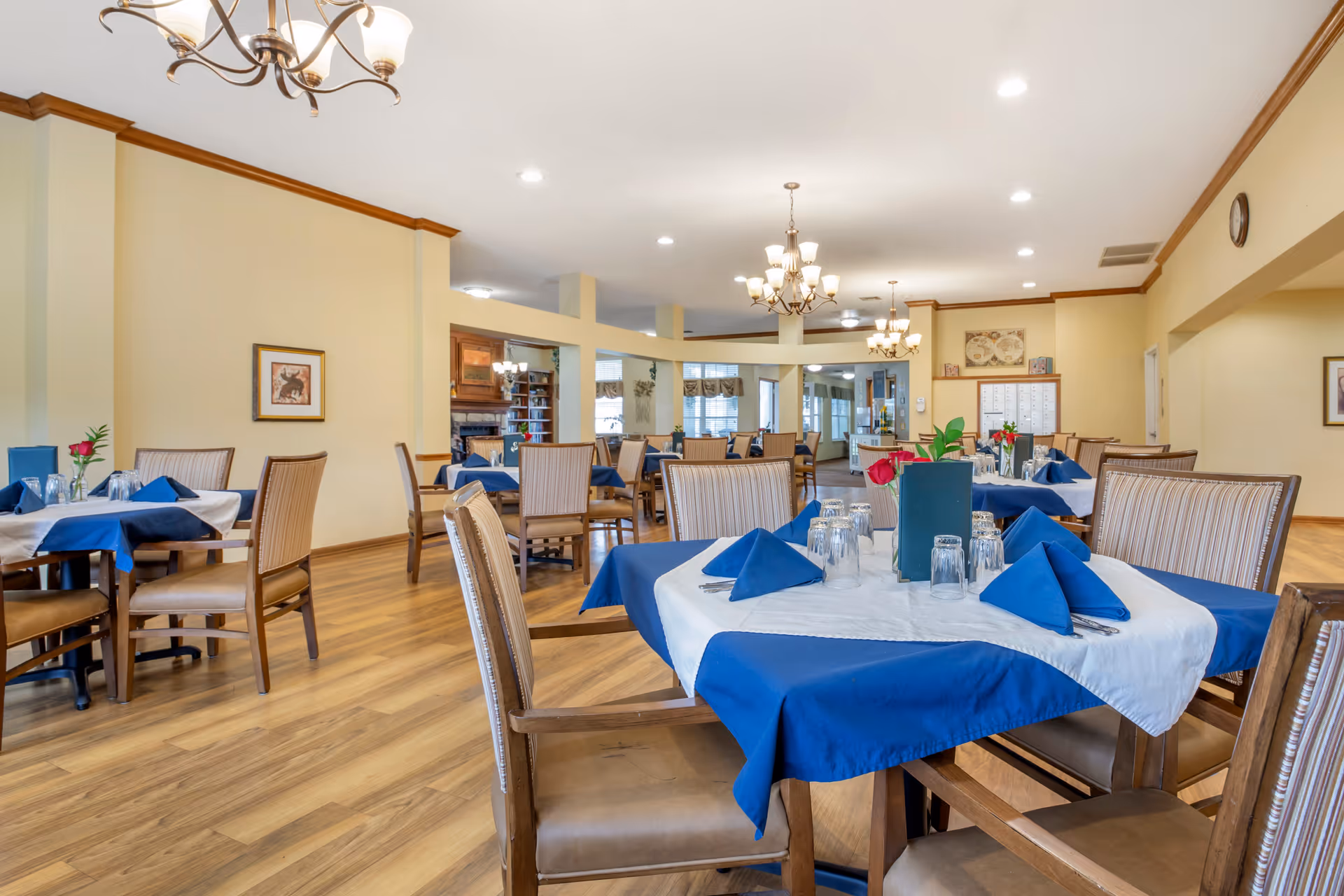Spacious dining room with tables set with blue tablecloths and napkins, chairs, and chandeliers.