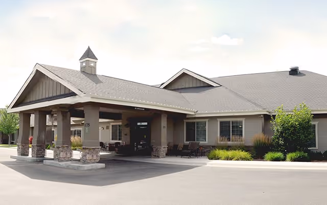 Front exterior of a single-story senior living facility with a covered porte-cochère entrance, seating area, and landscaped greenery.