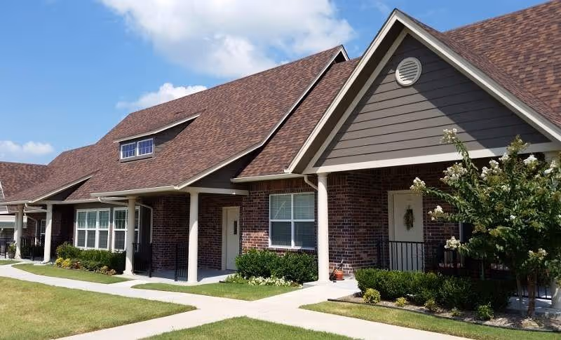 Brick senior living facility with multiple entrances and neatly kept landscaping along a sidewalk.
