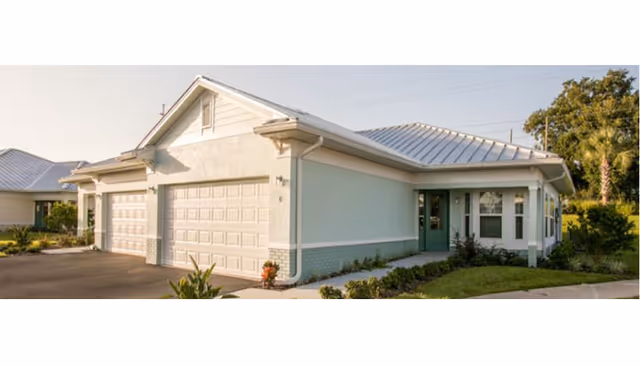Single-story light blue building with a metal roof, three-car garage, driveway and landscaped front lawn.