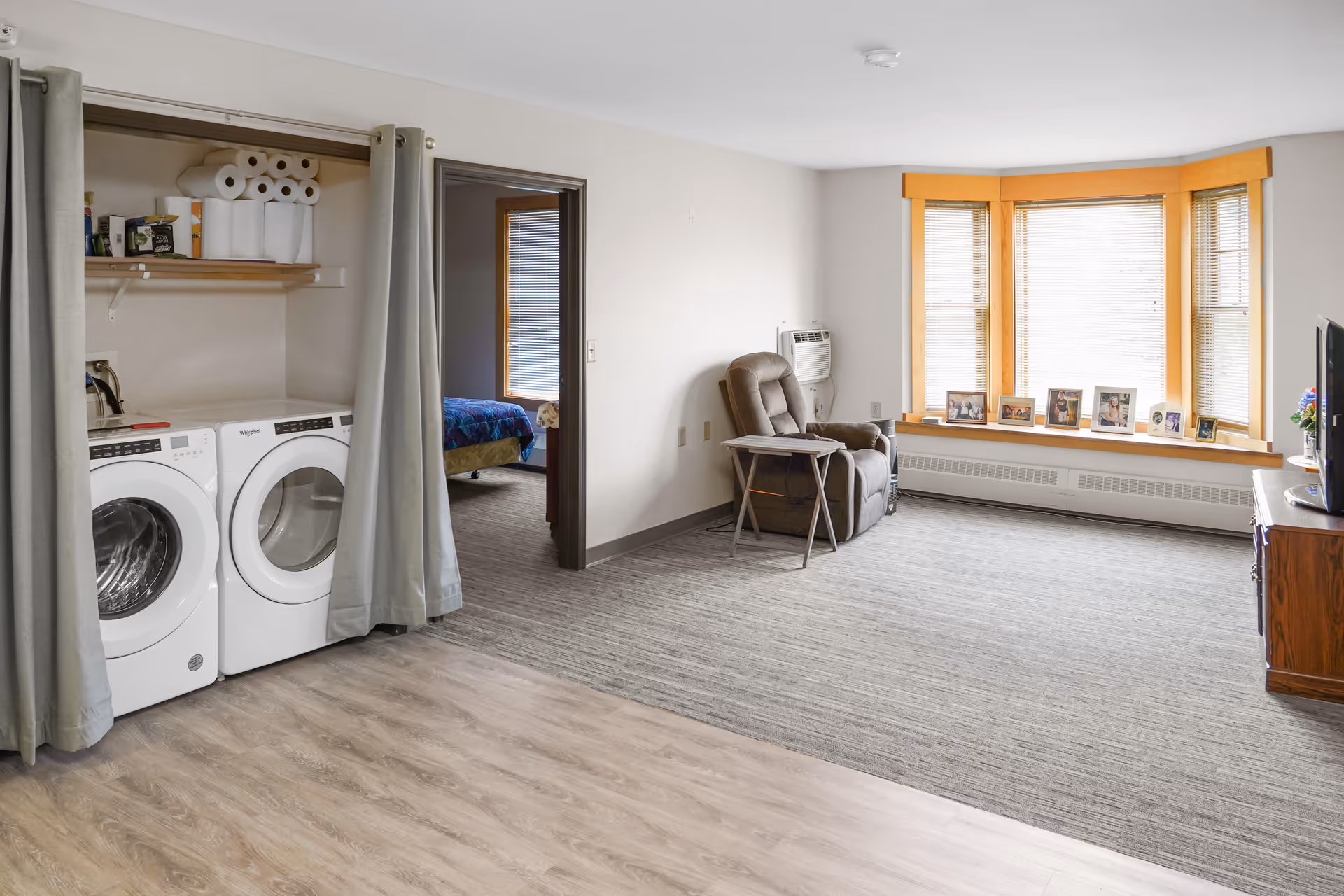 Spacious living room with a recliner by a bay window and a washer-dryer alcove concealed by curtains.