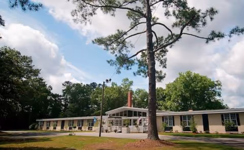 Single-story senior living facility exterior with a covered entrance and tall trees.