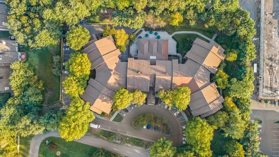 Aerial view of a tree-surrounded senior living building with a circular driveway and parked cars.