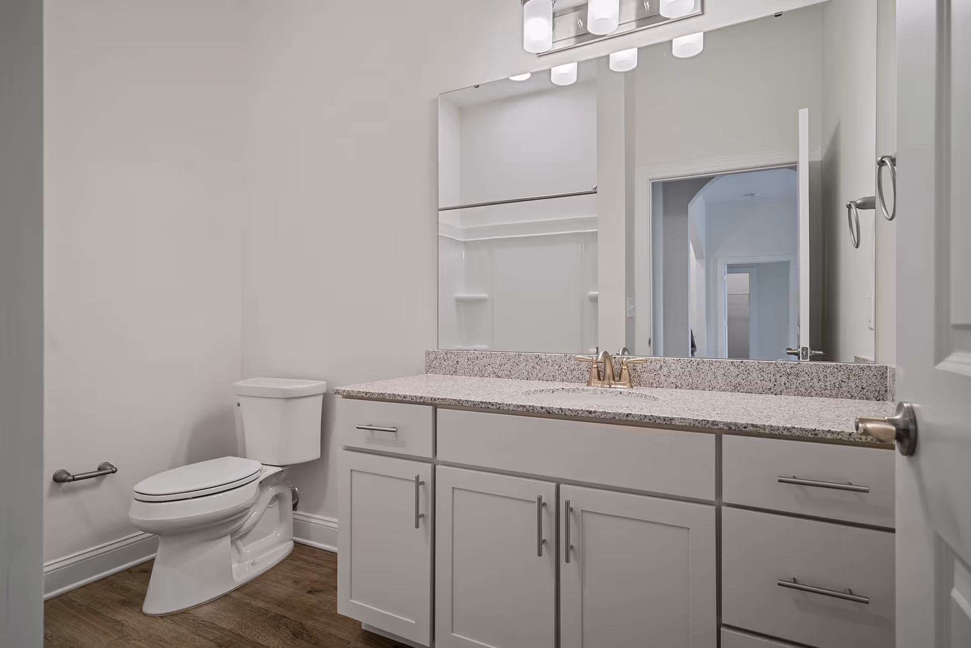A clean modern bathroom featuring a white vanity with a granite countertop and large mirror, plus a toilet.