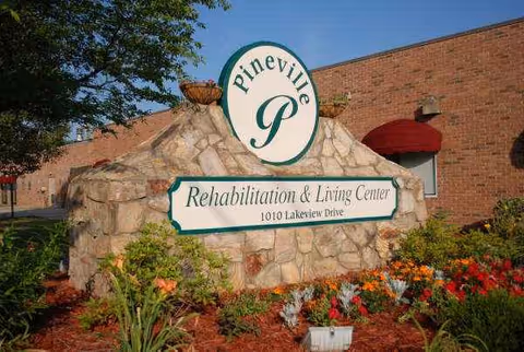 Stone sign for Pineville Rehabilitation and Living Center with landscaping in front of brick building.