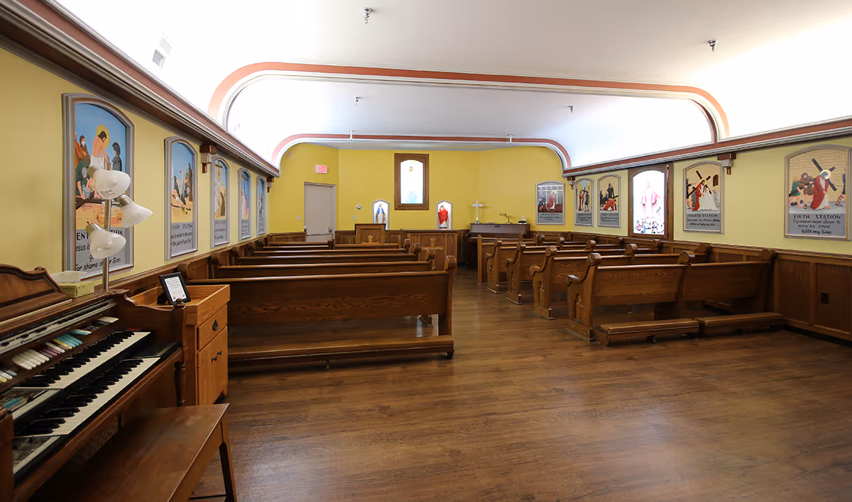 Interior chapel with wooden pews, an organ at left, and religious artwork along yellow walls.