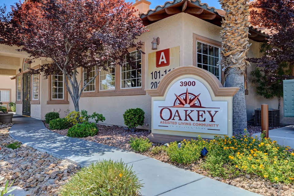 Exterior view of Oakey Assisted Living Community building with a landscaped walkway, trees, bushes, and a sign displaying the community name and address number 3900.