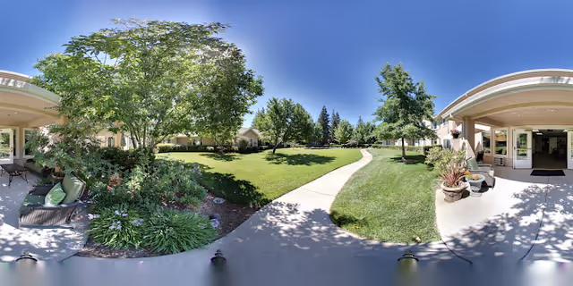 Sunny landscaped courtyard with a central walkway flanked by lawns, trees, and covered patio seating areas.