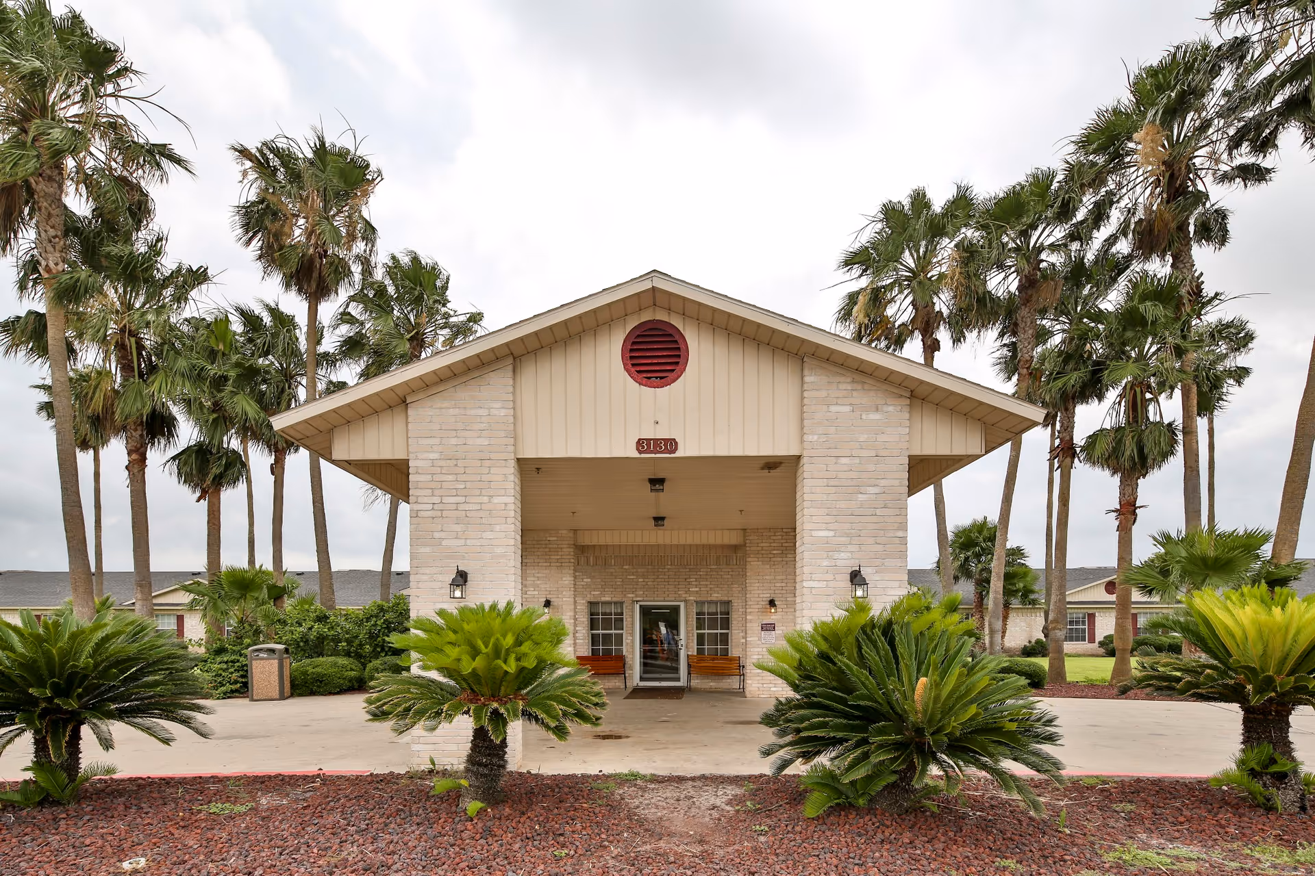 Front entrance of Kingsville Nursing and Rehabilitation Center with a covered porte-cochère, palm trees, and landscaped shrubs.